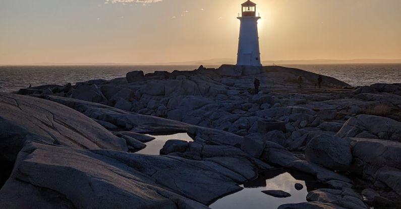 Mentorship Guidance - A lighthouse is on a rocky shore with the sun setting behind it