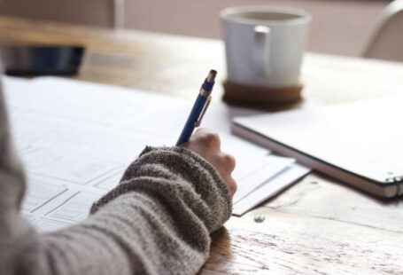 Resume Writing - person writing on brown wooden table near white ceramic mug