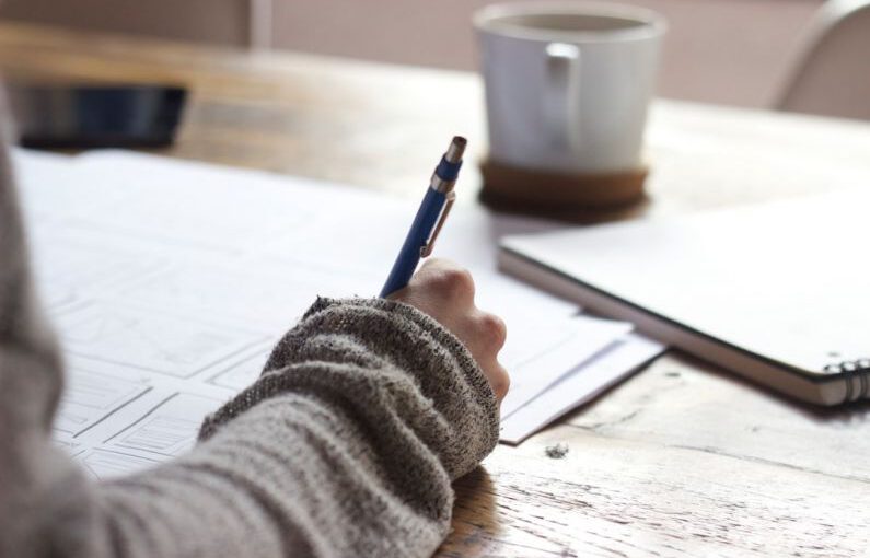 Resume Writing - person writing on brown wooden table near white ceramic mug